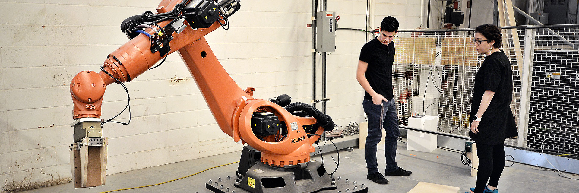 Students stand to the right of a large Kuka robot used for building prototypes.
