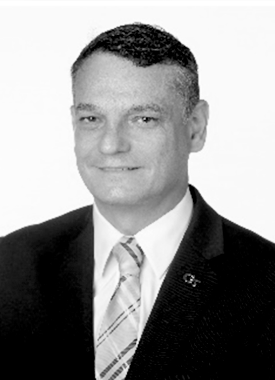 This is a grayscale portrait of Dr. Castro Lacouture. He is smiling towards the camera wearing a plaid tie and a Georgia Tech Lapel pin.