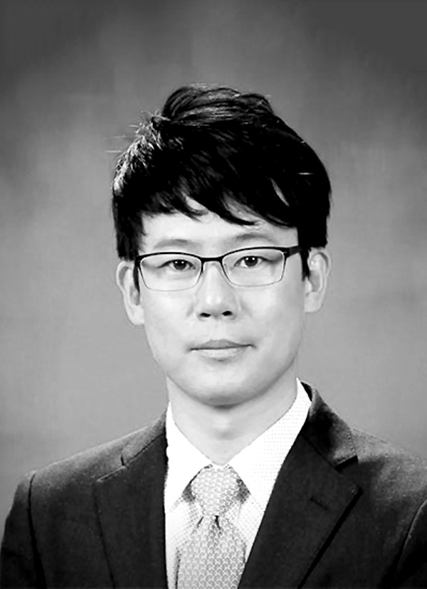 This is a grayscale portrait of Dr. lee. He is looking towards the camera wearing a dark suit and a tie.