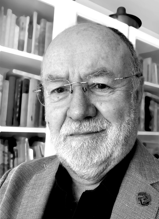 This is a grayscale portrait of John Mitchell, he is smiling towards the camera in front of a bookcase. He is wearing a buildingSMART lapel pin.