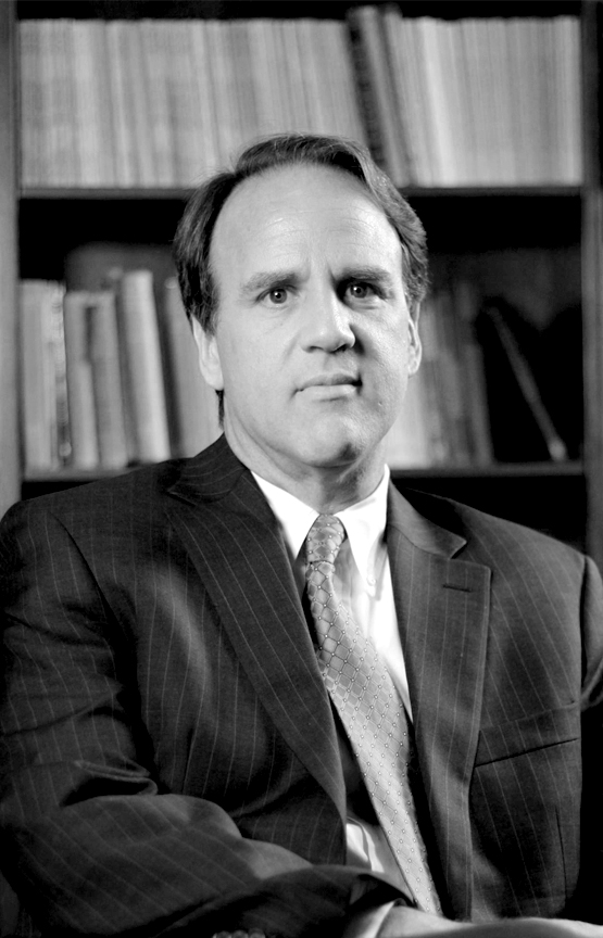 This is a soft-light portrait of Dr. Soibelman in grayscale. He is wearing a pinstripe suit and there are bookshelves visible in the background. 